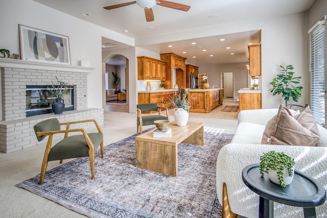 living area featuring light carpet, arched walkways, ceiling fan, a brick fireplace, and recessed lighting