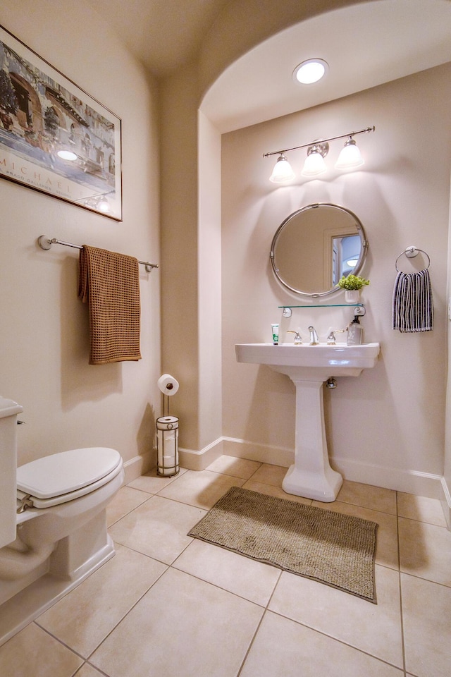 half bath with baseboards, toilet, and tile patterned floors