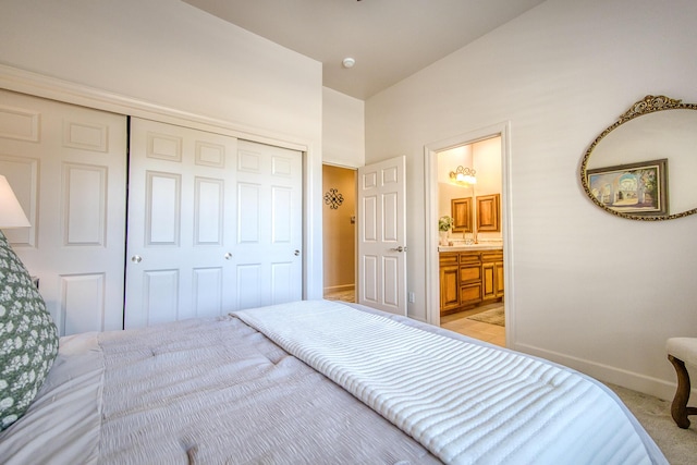 bedroom featuring a closet, light colored carpet, baseboards, and ensuite bathroom