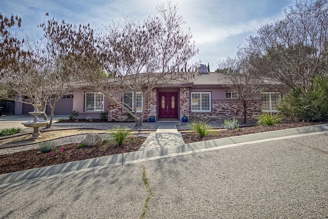 ranch-style home featuring a garage, a chimney, concrete driveway, and stucco siding