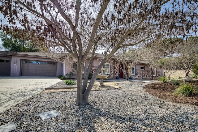 ranch-style house with an attached garage, stone siding, concrete driveway, and stucco siding