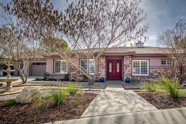 single story home featuring a garage, stucco siding, a chimney, and brick siding