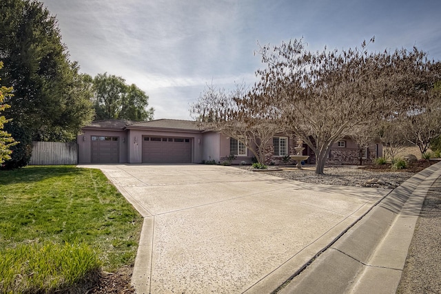 view of front of house featuring an attached garage, fence, driveway, stucco siding, and a front yard