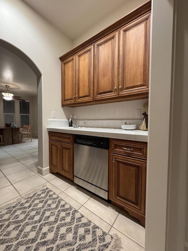 kitchen featuring tile countertops, arched walkways, dishwasher, and light tile patterned flooring