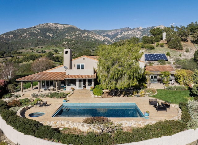 back of house with a tile roof, an outdoor pool, a patio area, and a mountain view