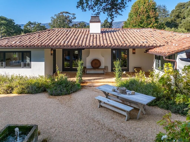 rear view of property with a tile roof, a patio, a chimney, and stucco siding