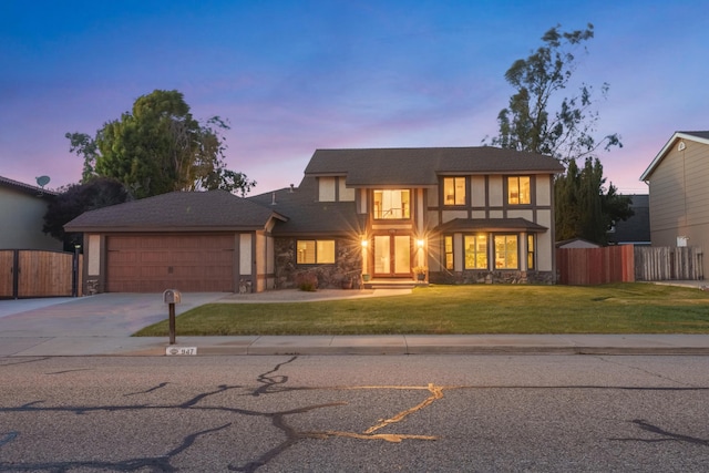 english style home featuring fence, a yard, concrete driveway, a garage, and stone siding