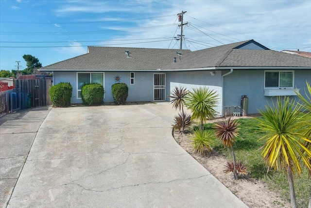 ranch-style home with a shingled roof, fence, and stucco siding