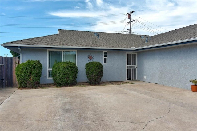 back of property with roof with shingles, fence, and stucco siding