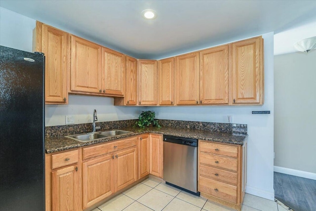 kitchen featuring freestanding refrigerator, light tile patterned flooring, a sink, dark stone countertops, and dishwasher