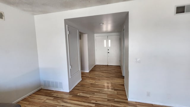 corridor featuring visible vents, baseboards, and wood finished floors