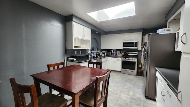 kitchen featuring a skylight, open shelves, dark countertops, appliances with stainless steel finishes, and white cabinetry