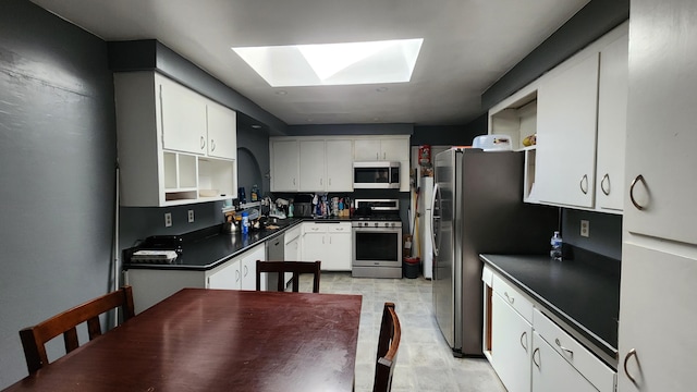 kitchen with a skylight, white cabinets, appliances with stainless steel finishes, open shelves, and dark countertops