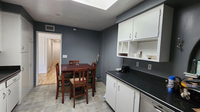 kitchen with white dishwasher, dark countertops, visible vents, and white cabinets