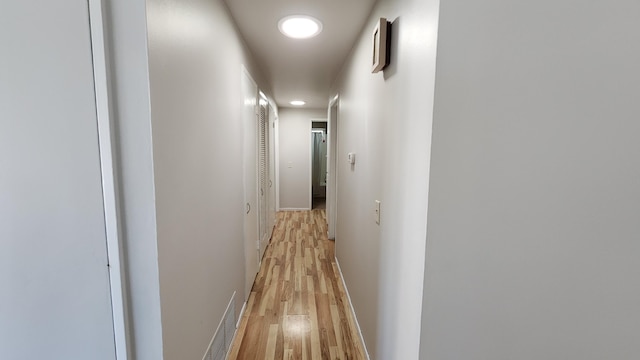 hall featuring light wood-style flooring, visible vents, and baseboards