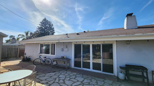 rear view of property featuring roof with shingles, a chimney, stucco siding, a patio area, and fence