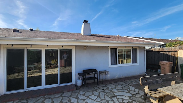 back of property with a chimney, stucco siding, a shingled roof, a patio area, and fence