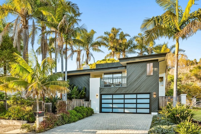 contemporary home with a garage, decorative driveway, a balcony, and fence