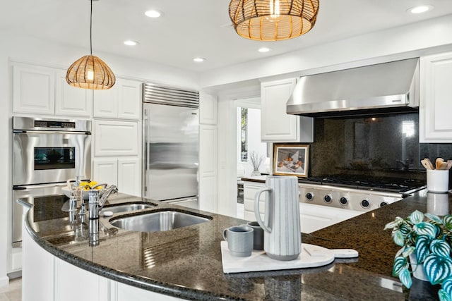 kitchen with dark stone countertops, appliances with stainless steel finishes, pendant lighting, and wall chimney exhaust hood