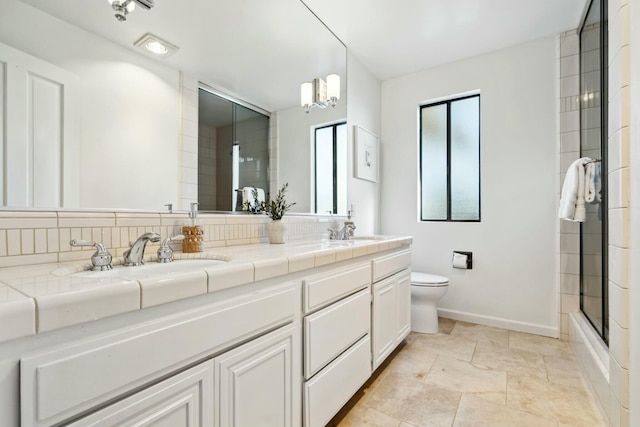 bathroom featuring double vanity, toilet, baseboards, and a sink