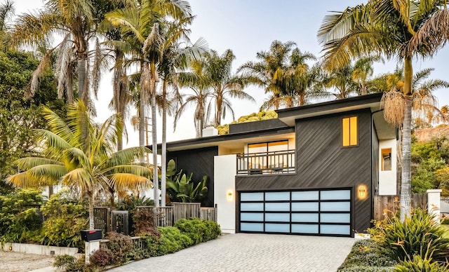 view of front of house with a balcony, decorative driveway, fence, and a garage