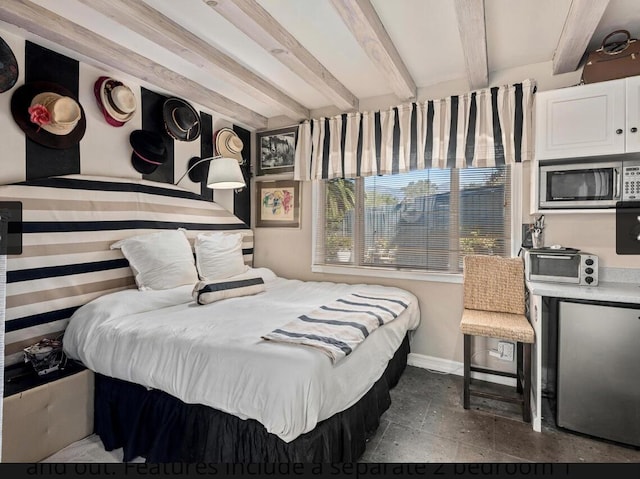 bedroom featuring a toaster, baseboards, stainless steel refrigerator, beamed ceiling, and stone tile flooring