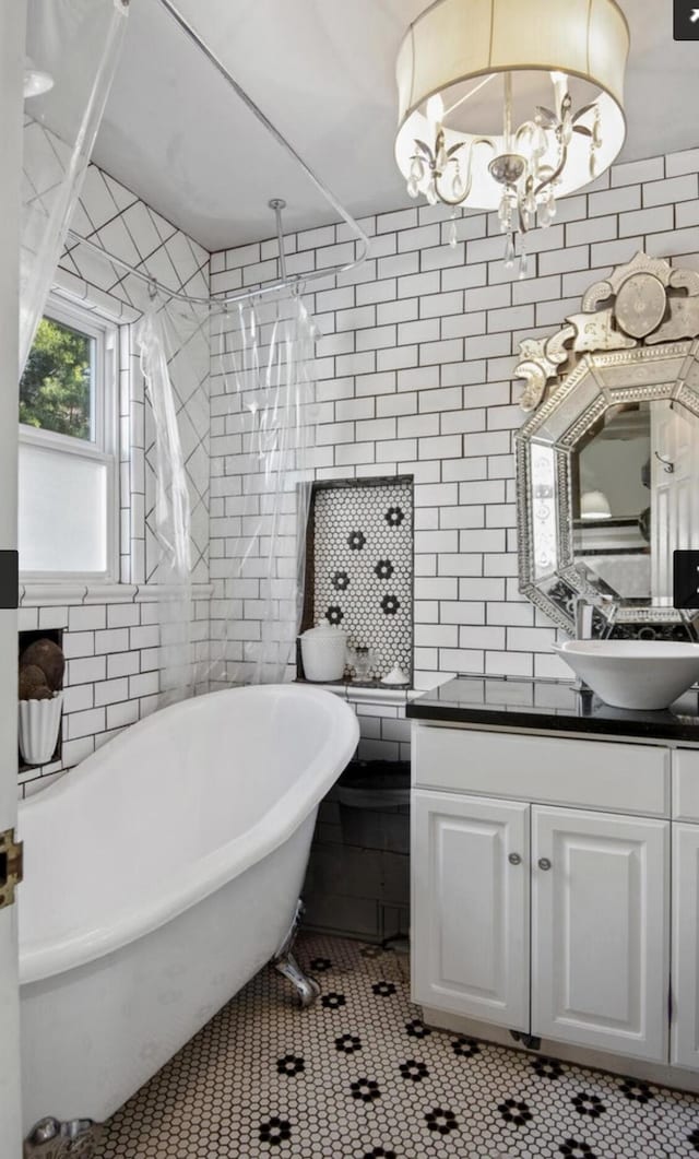 bathroom featuring tile patterned flooring, vanity, tile walls, a soaking tub, and an inviting chandelier