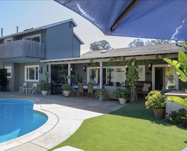 back of property featuring a lawn, a patio area, a balcony, and an outdoor pool