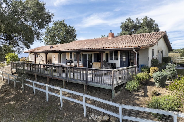 back of house featuring a chimney, stucco siding, fence, a deck, and a tiled roof