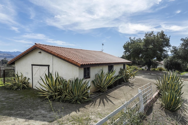 view of home's exterior with a tiled roof, fence, an outdoor structure, and stucco siding