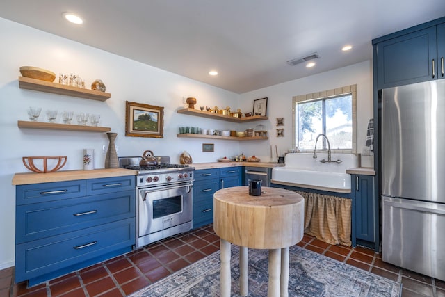 kitchen with appliances with stainless steel finishes, blue cabinets, a sink, and wood counters