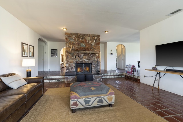 tiled living area with arched walkways, a stone fireplace, and visible vents