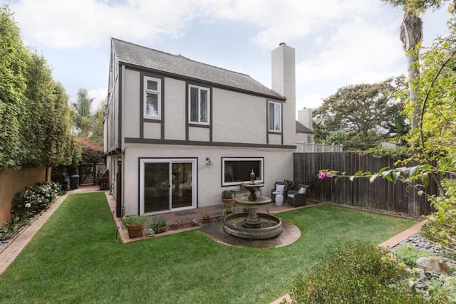 back of property featuring a lawn, a chimney, a fenced backyard, and stucco siding