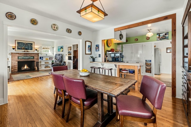 dining area featuring a brick fireplace and light wood-style flooring