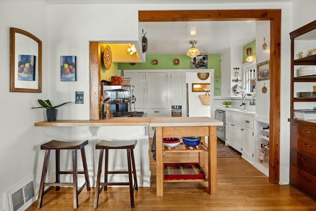 kitchen featuring visible vents, stainless steel dishwasher, white cabinets, wood finished floors, and a kitchen bar