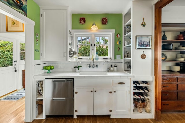 kitchen with tile counters, white cabinets, a sink, and wood finished floors