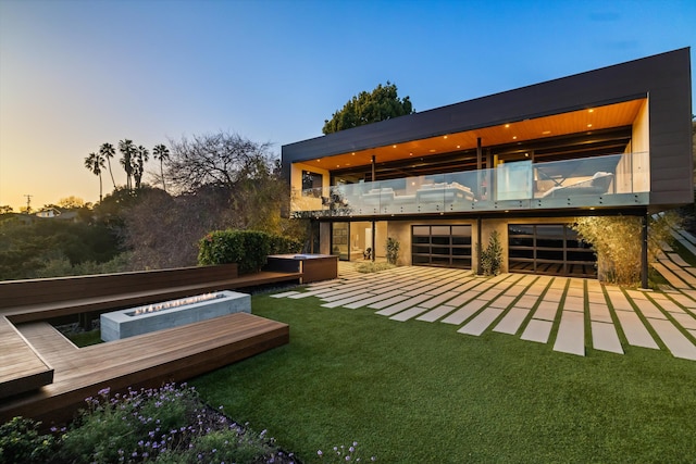 back of house at dusk with a balcony, a patio area, a deck, a jacuzzi, and a lawn