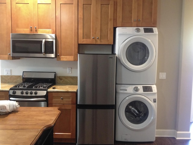 kitchen with stacked washer / drying machine, baseboards, appliances with stainless steel finishes, and brown cabinets