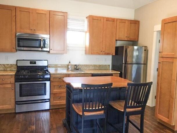 kitchen with dark wood-type flooring, light countertops, brown cabinetry, stainless steel appliances, and a sink