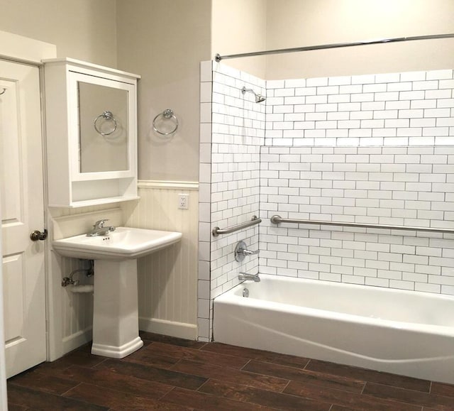 bathroom featuring bathtub / shower combination, a sink, wainscoting, and wood finish floors