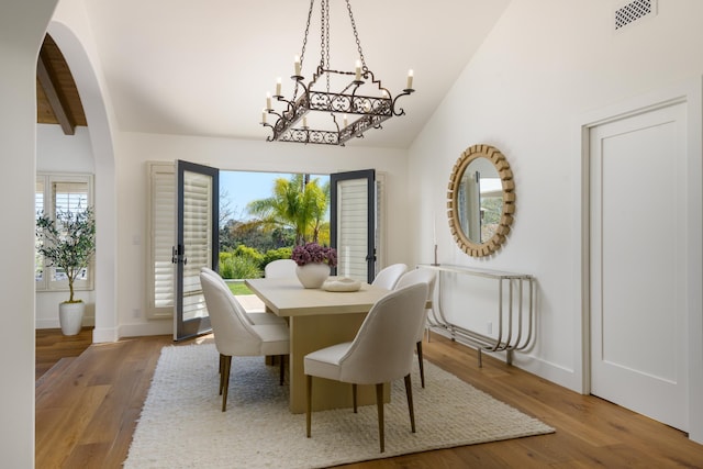 dining space with lofted ceiling, visible vents, a chandelier, arched walkways, and wood finished floors
