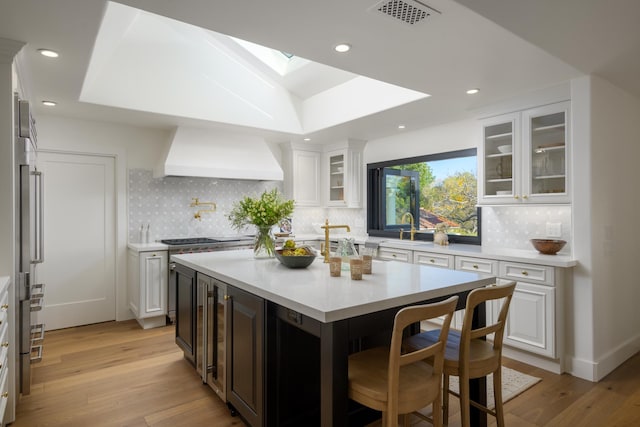 kitchen featuring a kitchen breakfast bar, white cabinetry, light countertops, premium range hood, and a skylight