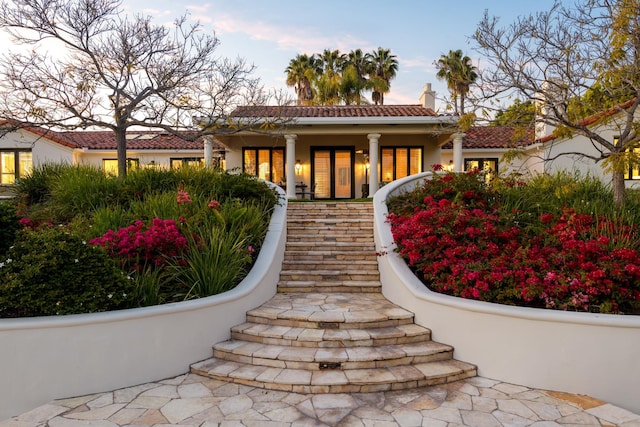 view of front facade with a porch, stucco siding, a tiled roof, and stairs