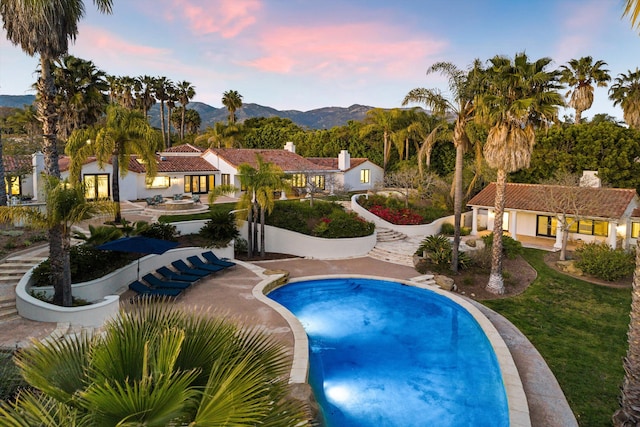 pool at dusk featuring a mountain view, fence, a patio area, and an outdoor pool