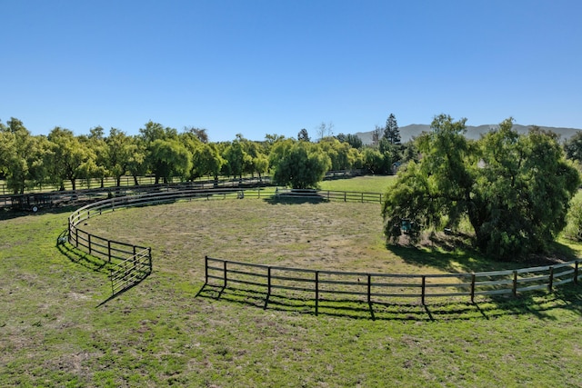 view of property's community with a mountain view, a rural view, a lawn, and fence