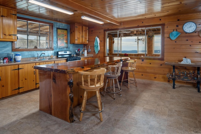 kitchen featuring a kitchen island, wood ceiling, stainless steel gas stove, and wood walls