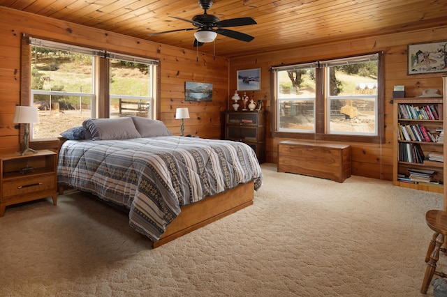 carpeted bedroom with a ceiling fan, wooden ceiling, and wood walls