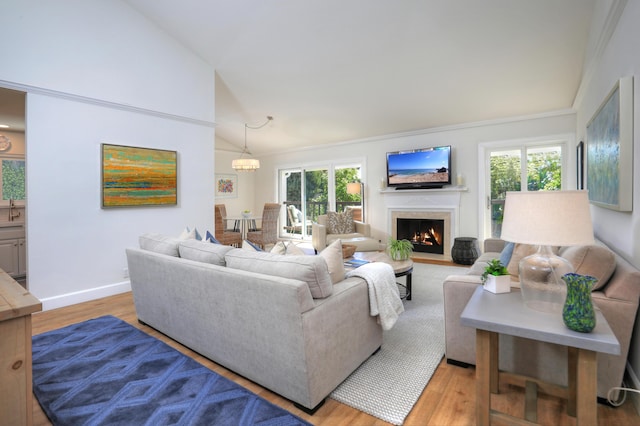 living area with baseboards, a chandelier, a fireplace with flush hearth, light wood-style floors, and high vaulted ceiling