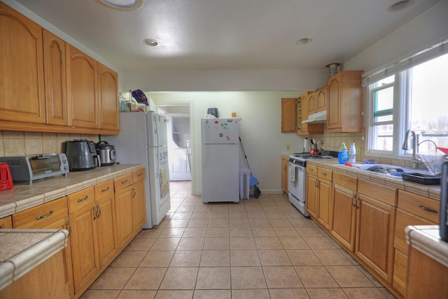 kitchen featuring a toaster, tile counters, a sink, white appliances, and under cabinet range hood