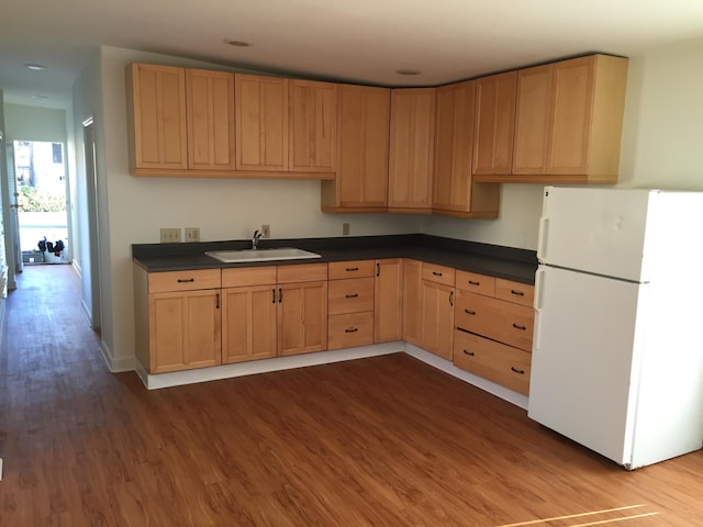 kitchen with dark wood-type flooring, freestanding refrigerator, a sink, and dark countertops